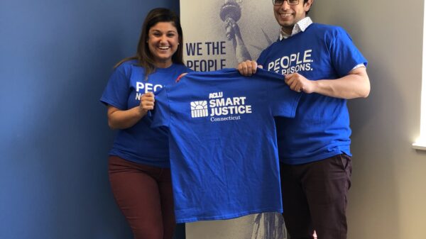 Melvin Medina and Sandy Lomonico, ACLU Smart Justice Connecticut, hold "people not prisons" shirts in front of ACLU-CT banner