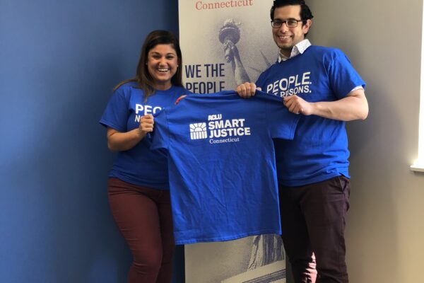 Melvin Medina and Sandy Lomonico, ACLU Smart Justice Connecticut, hold "people not prisons" shirts in front of ACLU-CT banner