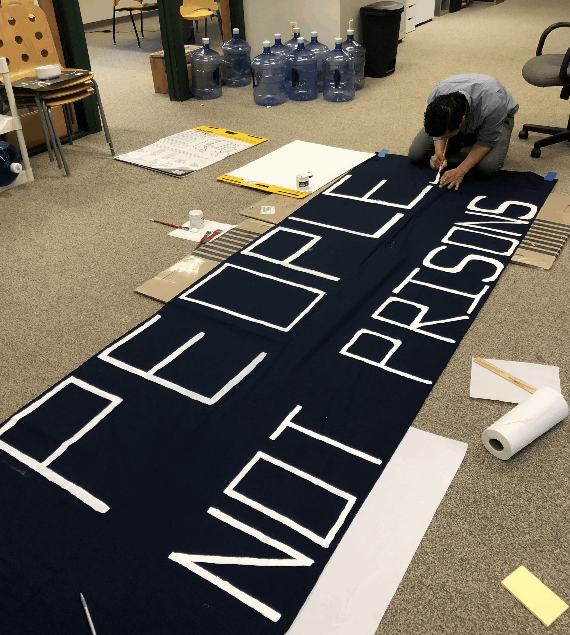 ACLU-CT staff member crouches with a paint brush over a banner that says