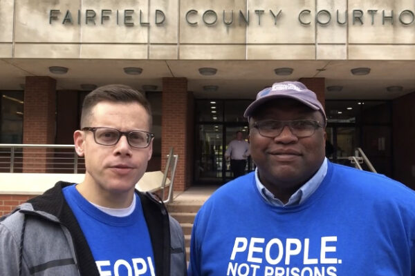 ACLU-CT Gus Marks-Hamilton and Anderson Curtis in blue "people, not prisons" shirts, stand outside of the Fairfield County Courthouse