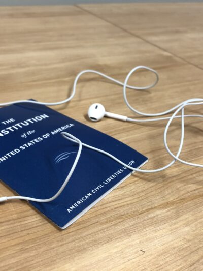 A blue Constitution of the United States, published by the ACLU, sits on a table under white headphones
