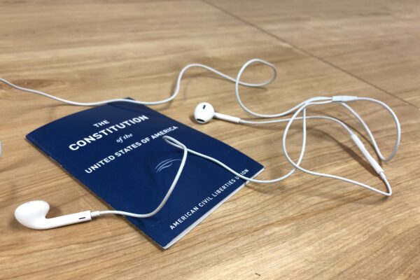 A blue Constitution of the United States, published by the ACLU, sits on a table under white headphones
