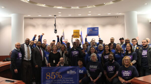 ACLU of Connecticut Smart Justice, CONECT, GHIAA, and Connecticut state legislators stand and sit in a group to support Clean Slate, behind a blue banner with a statistic about voters' support for Clean Slate ideas.