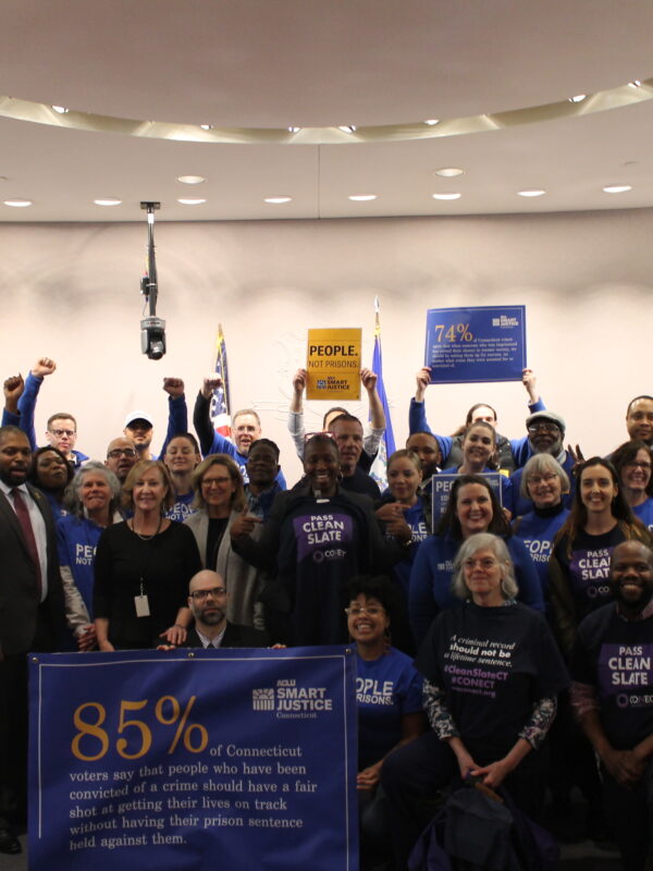 ACLU of Connecticut Smart Justice, CONECT, GHIAA, and Connecticut state legislators stand and sit in a group to support Clean Slate, behind a blue banner with a statistic about voters' support for Clean Slate ideas.