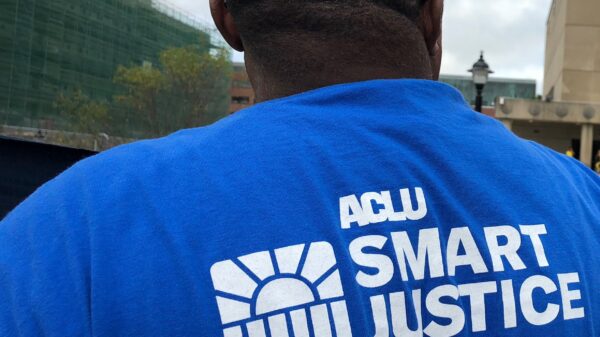 From behind, a man stands in a blue ACLU of Connecticut Smart Justice shirt