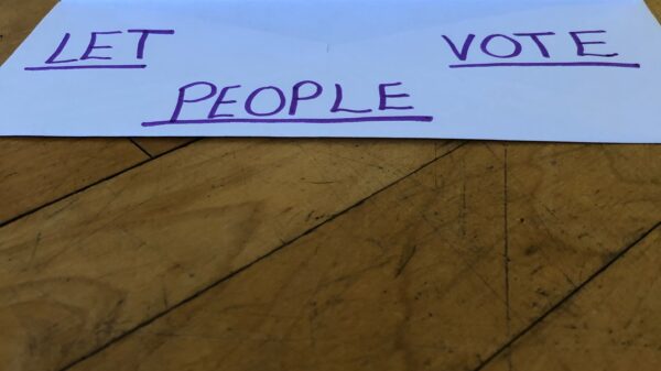 a white envelope against wood background. written on the envelope: LET PEOPLE VOTE