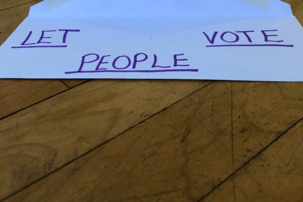 a white envelope against wood background. written on the envelope: LET PEOPLE VOTE