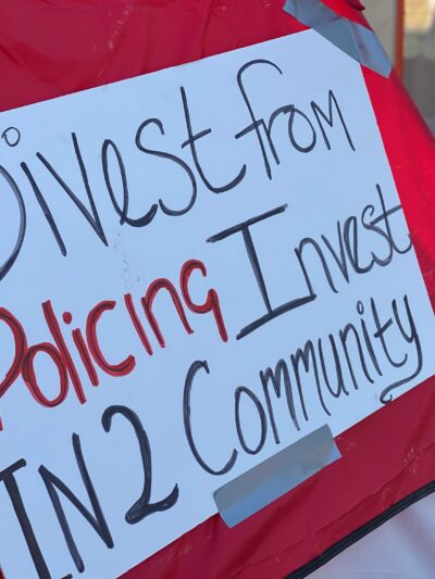 Red tent with white sign. Sign reads: Divest from policing / invest in2 community