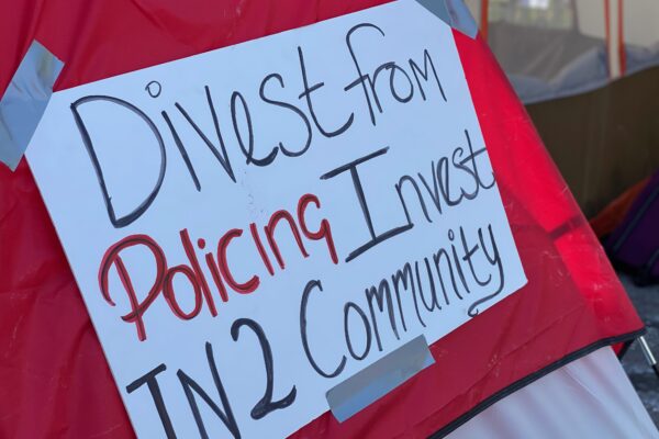 Red tent with white sign. Sign reads: Divest from policing / invest in2 community