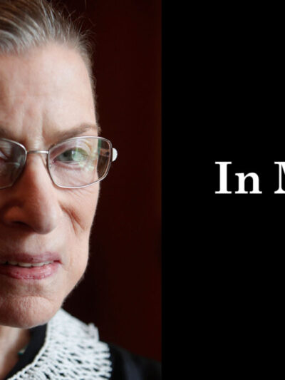 A close up photo of Supreme Court Justice Ruth Bader Ginsburg is on the left. She is looking directly at the camera. On the right, a black box. In the box, "in memory" is written in white letters.