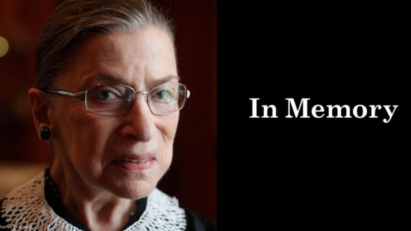 A close up photo of Supreme Court Justice Ruth Bader Ginsburg is on the left. She is looking directly at the camera. On the right, a black box. In the box, "in memory" is written in white letters.
