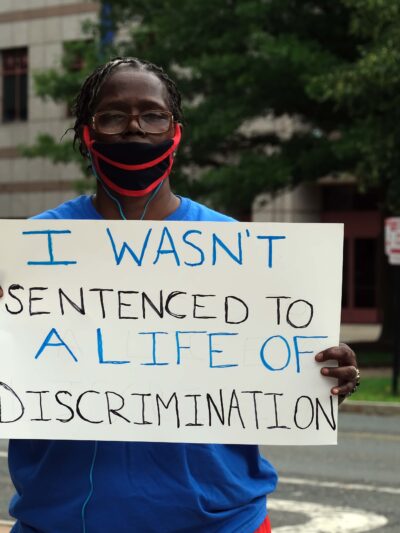 ACLU-CT Smart Justice leader stands with sign: I wasn't sentenced to a life of discrimination