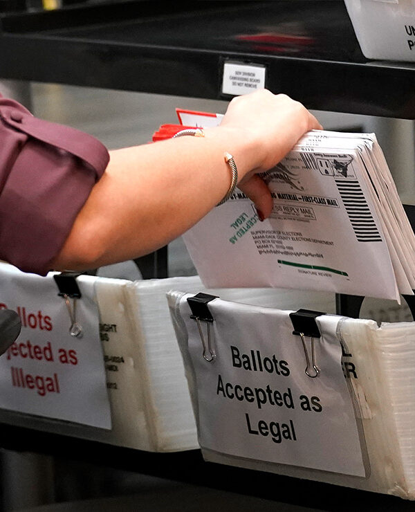 An election worker sorts vote-by-mail ballots in bins.