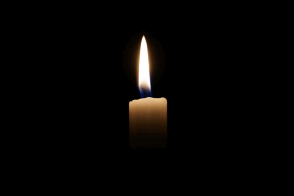 a white candle, lit, is in the center of the frame. The rest of the image is a black square
