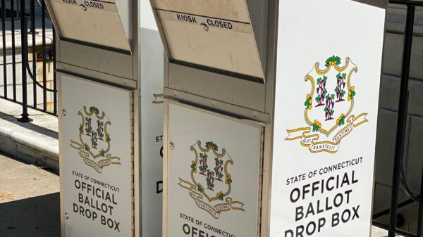 Two official Connecticut ballot drop boxes sit outside of the Waterbury city hall in 2020. The boxes are large, rectangular, and look like library book drops, with the state of CT seal visible, and "official ballot drop box," on their fronts and sides