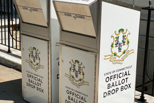 Two official Connecticut ballot drop boxes sit outside of the Waterbury city hall in 2020. The boxes are large, rectangular, and look like library book drops, with the state of CT seal visible, and "official ballot drop box," on their fronts and sides