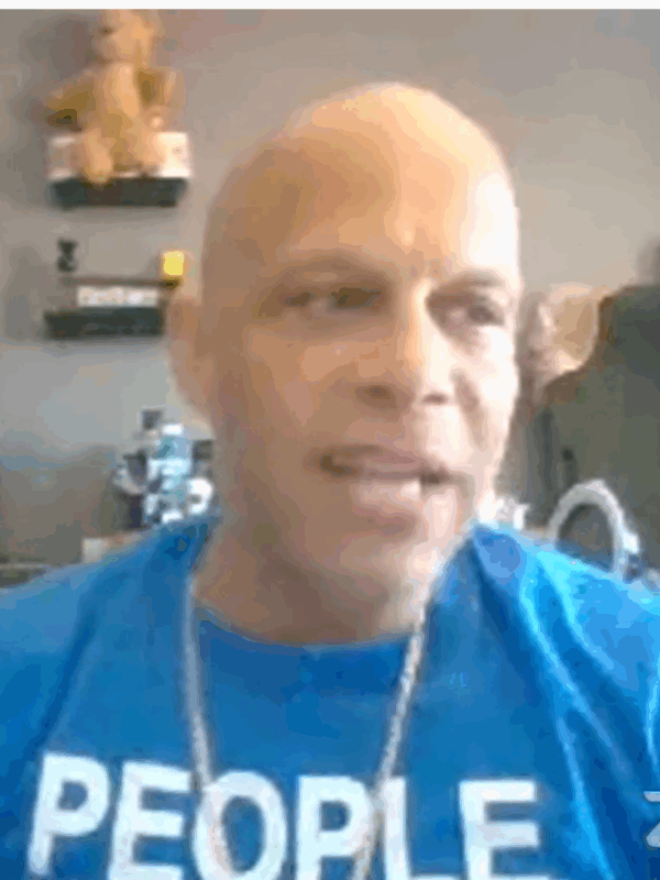ACLU-CT Smart Justice leader Brian Sullivan testifies before the judiciary committee March 22, 2021. He is seated + wearing a blue people not prisons shirt, looking slightly to the right. Behind him is a Black Lives Matter shirt on a wall.