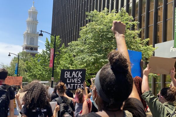 Protesters march in Hartford to call for the state to value Black lives. In the foreground, a person has their fist up. In the background, a Black Lives Matter sign