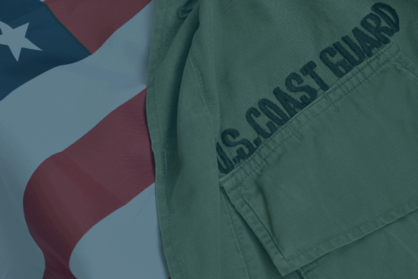 On the right, part of a U.S. Coast Guard uniform is visible, with "U.S. Coast Guard" stitching prominent. On the left and behind the uniform is the U.S.A. flag