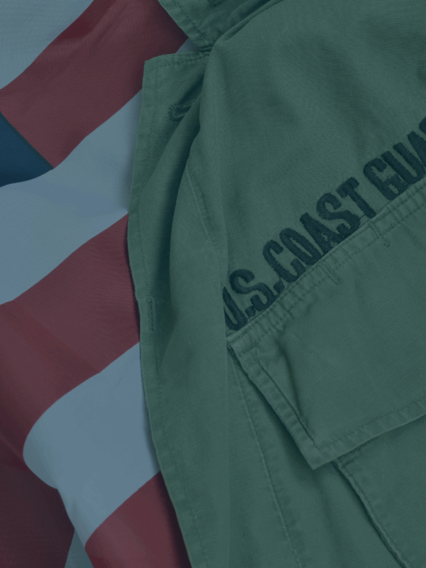 On the right, part of a U.S. Coast Guard uniform is visible, with "U.S. Coast Guard" stitching prominent. On the left and behind the uniform is the U.S.A. flag