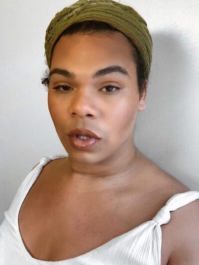 Erycka Ortiz, ACLU of Connecticut field organizer, stands facing the camera. She is wearing a green head wrap and a white top, and she is looking straight at the camera.