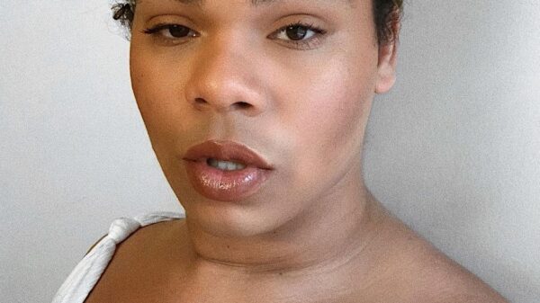 Erycka Ortiz, ACLU of Connecticut field organizer, stands facing the camera. She is wearing a green head wrap and a white top, and she is looking straight at the camera.