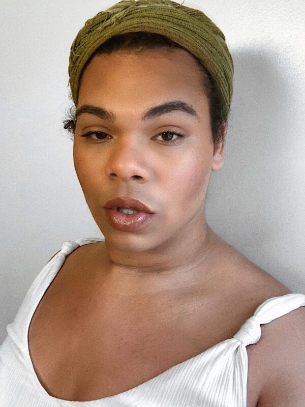 Erycka Ortiz, ACLU of Connecticut field organizer, stands facing the camera. She is wearing a green head wrap and a white top, and she is looking straight at the camera.