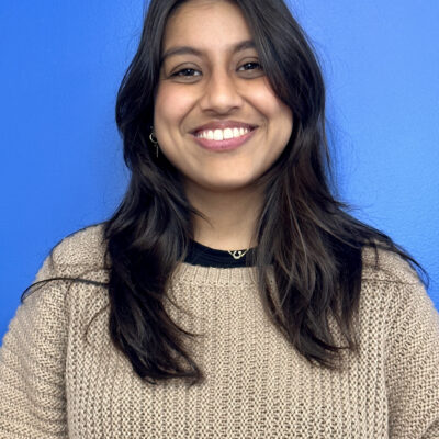 Sapana Anand standing in front of a blue background, smiling
