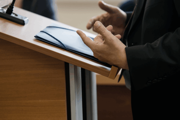an individual standing at a podium speaking, only their hands and the podium are visable