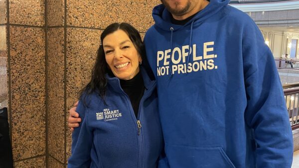 ACLUCT Smart Justice leaders Will and L stand at the capitol, smiling and wearing people not prisons blue hoodies