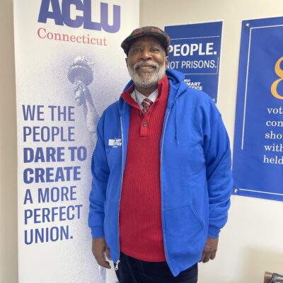 Smart Justice Leader Curtis Hudson standing and smiling next to an ACLU of CT poster