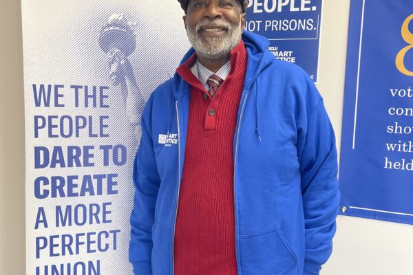 Smart Justice Leader Curtis Hudson standing and smiling next to an ACLU of CT poster