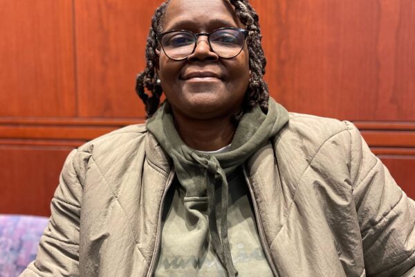 ACLU CT Smart Justice leader Terri Ricks sits, smiling at the camera and wearing a brown jacket and brown hoodie.