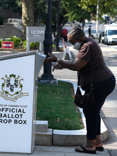 An Afrian-American woman drops a ballot into a State of Connecticut Official Ballot Drop Box outside Hartford City Hall.