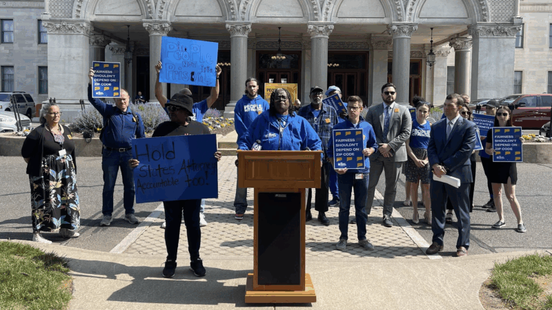 Smart Justice leaders are gathered in front of the Capitol to speak about prosecutorial accountability and one leader, in the center, stands at the podium as they speak.