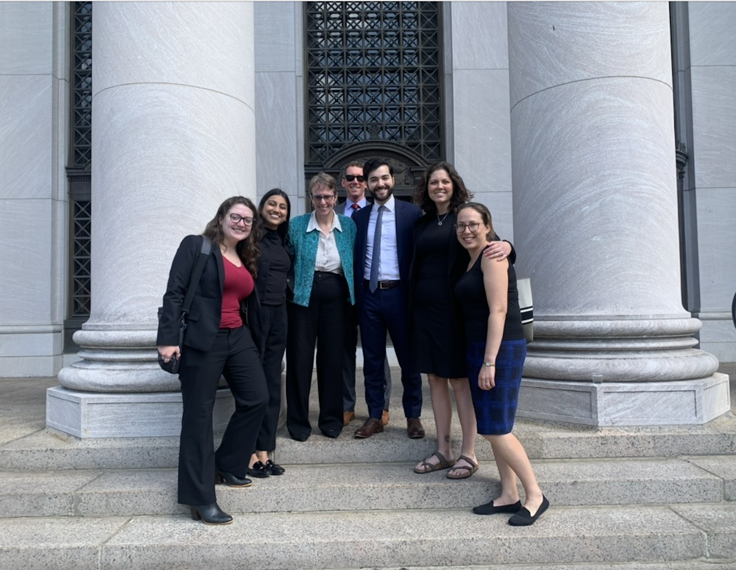In front of the court, our legal team plus co-counsel stands on the steps and smiles at the camera.