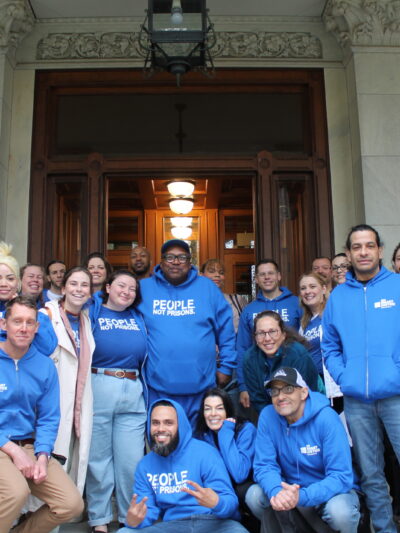 A group of approximately 20 people wearing ACLU bright blue t-shirts smiling at the camera, standing in front of the Capitol building in Hartford, Connecticut.