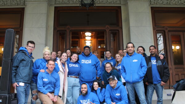 A group of approximately 20 people wearing ACLU bright blue t-shirts smiling at the camera, standing in front of the Capitol building in Hartford, Connecticut.