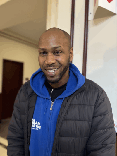 Chris, a Smart Justice Leader, is smiling at the camera wearing one of the smart justice zip ups.