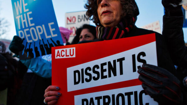 A white woman is in the crowd with a red sign that says "Dissent is Patriotic." Behind him is a blue sign that says, "WE THE PEOPLE."