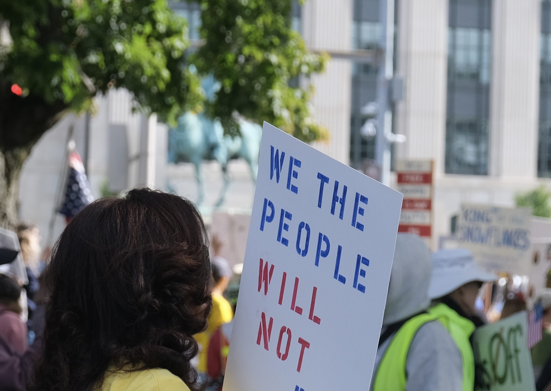 A woman in a crowd is holding a sign that says: "We the people will not be silenced."