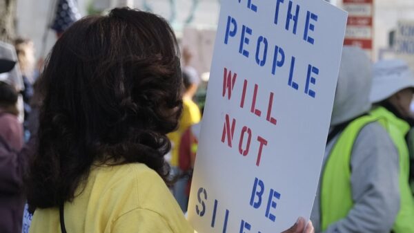 A woman in a crowd is holding a sign that says: "We the people will not be silenced."