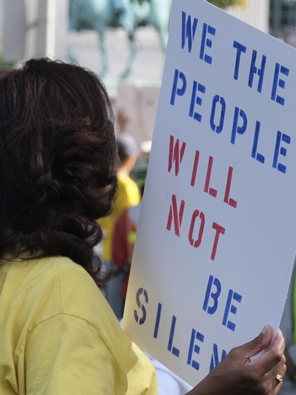 A woman in a crowd is holding a sign that says: "We the people will not be silenced."