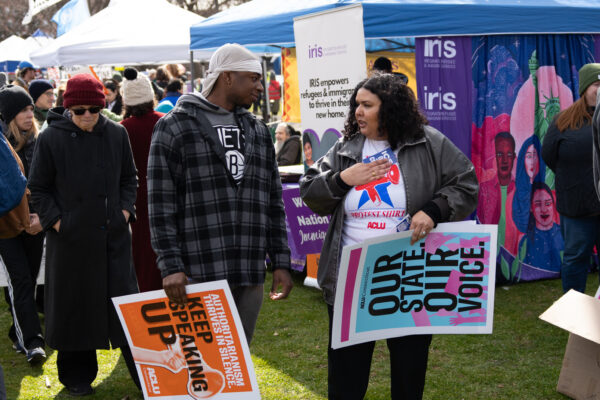 Cris, our community engagement program director, is speaking with a Black man in a flannel in the grass. Both are holding ACLU-branded signs that are orange and blue.