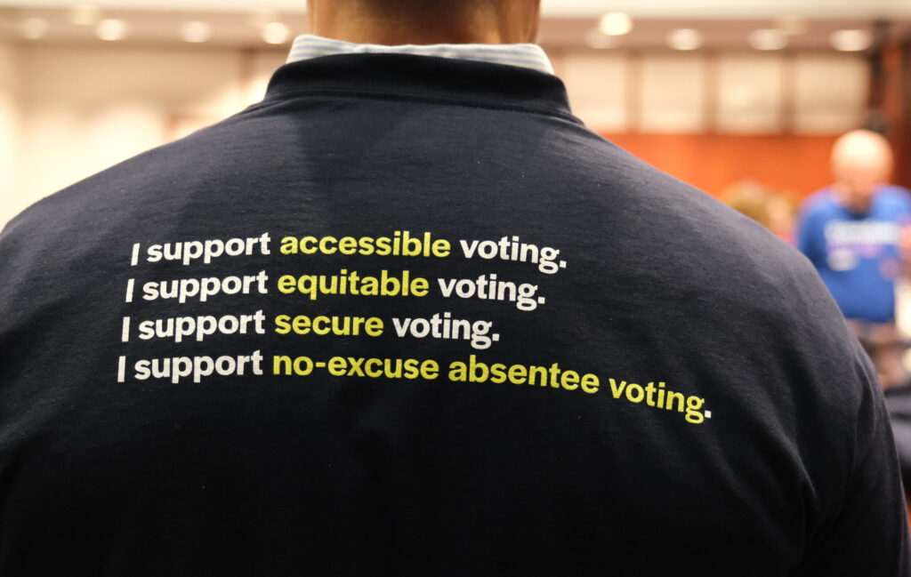 The back of Gus' shirt is navy blue and reads "I support accessible voting. I support equitable voting. I support secure voting. I support no-excuse absentee voting." in white.