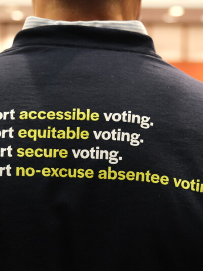 The back of Gus' shirt is navy blue and reads "I support accessible voting. I support equitable voting. I support secure voting. I support no-excuse absentee voting." in white.