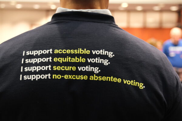 The back of Gus' shirt is navy blue and reads "I support accessible voting. I support equitable voting. I support secure voting. I support no-excuse absentee voting." in white.
