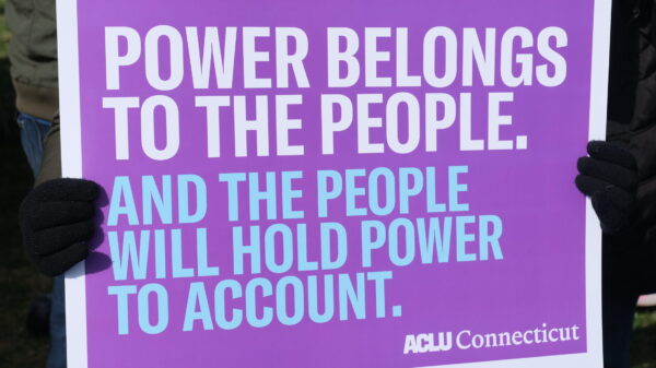 Zoomed in picture of a purple sign that says "Power belongs to the people." in white and below that text is "And the people will hold power to account." in blue.