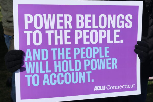 Zoomed in picture of a purple sign that says "Power belongs to the people." in white and below that text is "And the people will hold power to account." in blue.