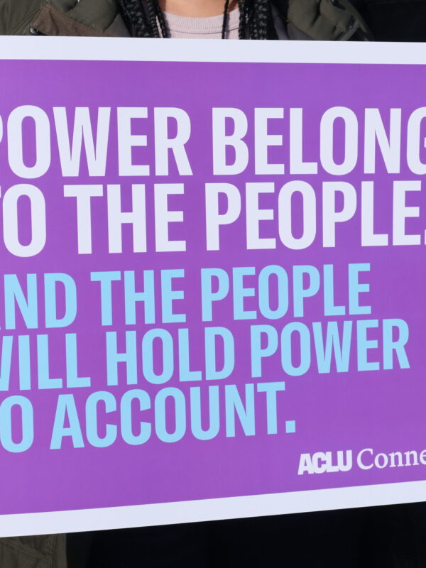 Zoomed in picture of a purple sign that says "Power belongs to the people." in white and below that text is "And the people will hold power to account." in blue.